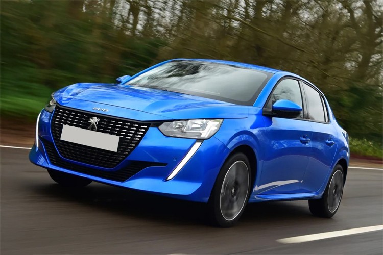 2024 Peugeot e-208 electric car in metallic blue color driving on a road, featuring LED headlights, sporty grille design, and aerodynamic profile, photographed in motion against blurred forest background