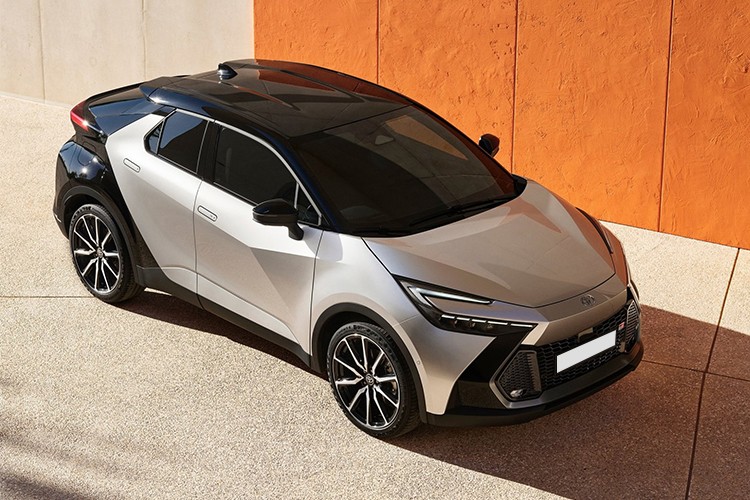 Top-side view of the Toyota C-HR in a striking silver and black two-tone finish, showcasing its bold and futuristic design, parked against a vibrant orange and white architectural backdrop.