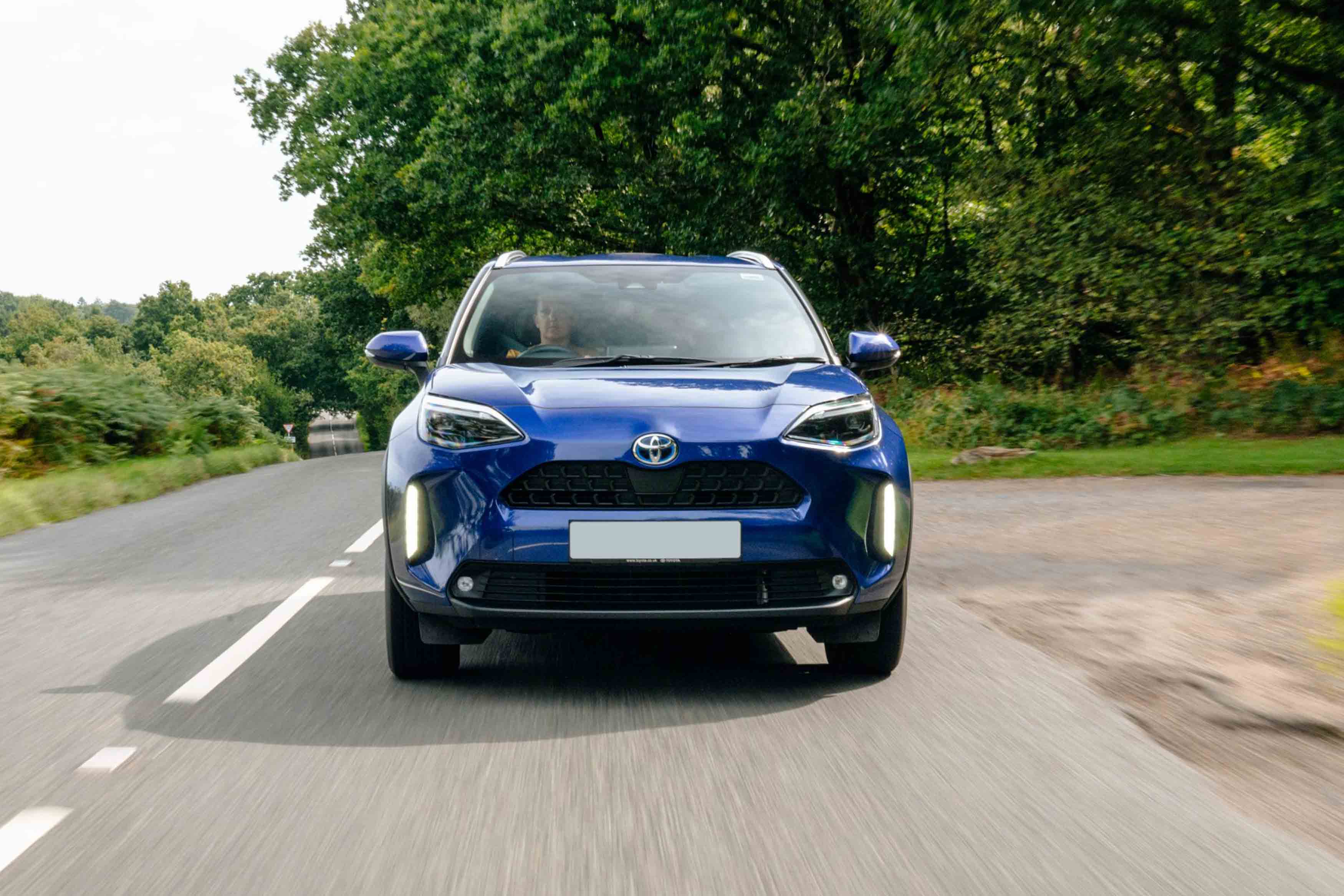 Toyota Yaris Cross Blue Toyota SUV driving on a rural road with hills in the background